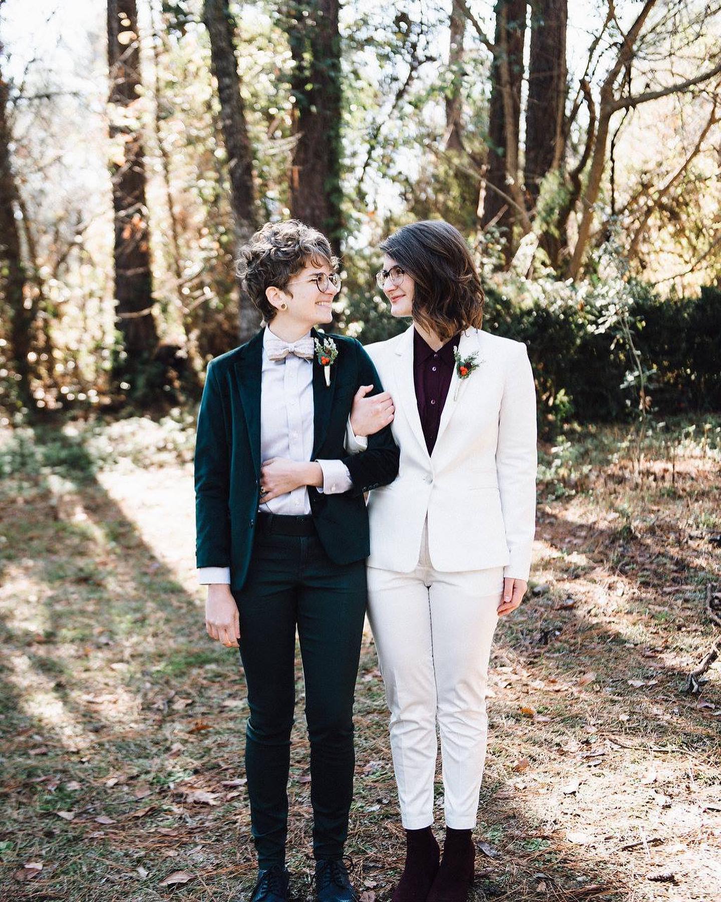 Two women in suits standing in a wooded area near a bridal salon.