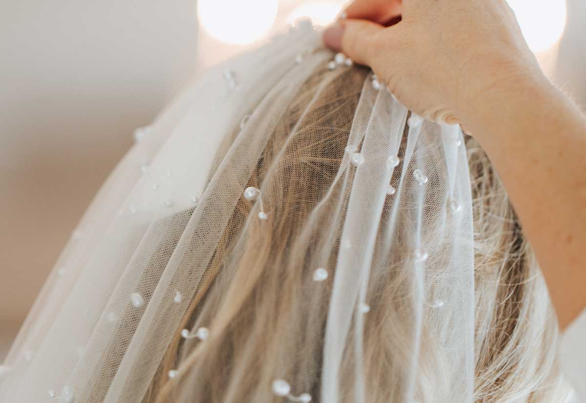 A bride putting on a veil with pearls.