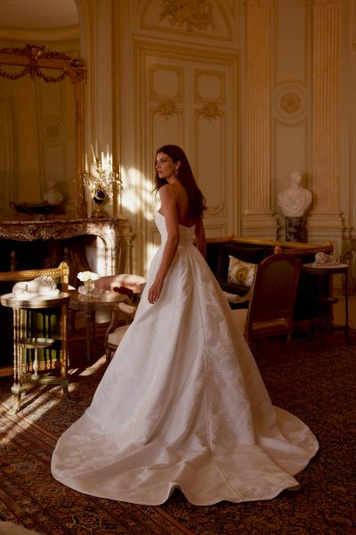 Back view of a woman in a dimly lit room wearing a ballgown wedding dress (wedding dress trends)