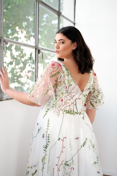 Back view of a woman wearing a wedding dress with colored, embroidered flowers. (wedding dress trends)