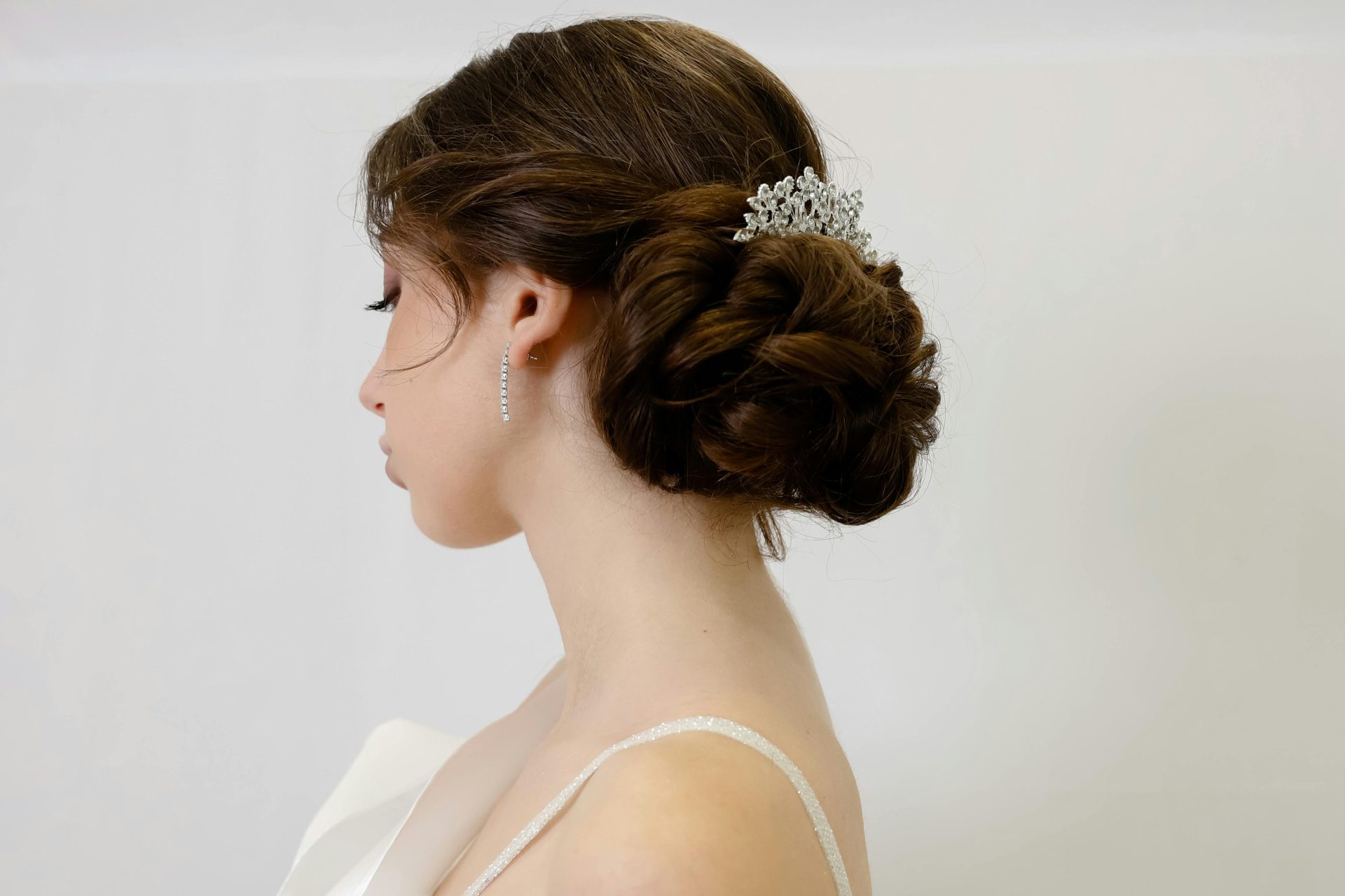 A brunette woman with a low bun accessorized with a sparkly hairpiece. (bridal accessories)